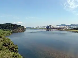 A vast and tranquil river in a clear day of fall. Apartment blocks and buildings under construction are seen at a distance.