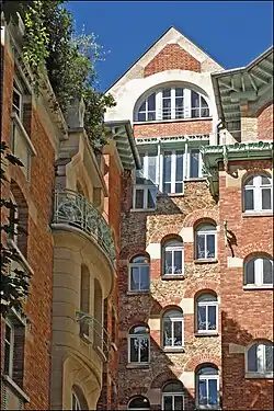 Photo en couleur deux deux façades de brique en angle rentrant avec encorbellements à gauche et fenêtres en escalier au fond