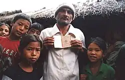 A Bhutanese man standing next to several children is depicted showing the camera his passport.