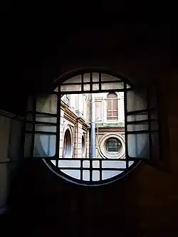 Imagen fotográfica de una claraboya circular, centrada en el cuadro. A través de la misma se ve un patio interno del edificio con más claraboyas que dan al aire y luz del edificio. La imagen se llama "Luz vs. oscuridad".