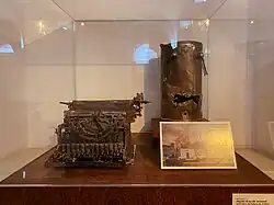 Máquina de escribir y máquina de café incineradas, rescatadas de los escombros del palacio dentro de una vitrina en exhibición en el Museo Nacional de Colombia.