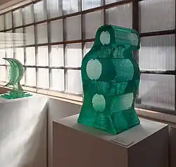 Dos esculturas de vidrio laminado en el MEVJG. En primer plano se observa Torso y a la izquierda se encuentra Cara de la Luna. La primera es una obra que une varias planchas de vidrio formando una estructura abstracta con círculos en medio que forman huecos vacíos. La segunda tiene forma de luna, de la que sobresale lateralmente la silueta de un rostro