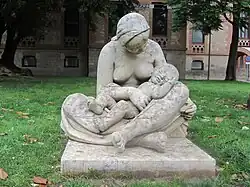 Escultura en piedra que representa una mujer con el pecho desnudo, sentada en el suelo con las piernas cruzadas y un niño en los brazos
