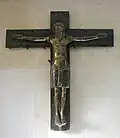 La Cruz de bronce de Minden (1170/1020): Cristo aunque con los ojos abiertos, de pie en lugar de colgado, sin herida en el costado, pero con signos de sufrimiento, el pecho hundido y las comisuras de la boca hacia abajo.
