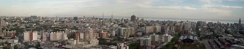 Foto Panorámica de los barrios Aguada, Centro y Cordón de Montevideo, tomada desde la torre de Antel. Se distingue el edificio de la intendencia de Montevideo (centro), el palacio Salvo (derecha) y la Estación Central General Artigas abajo a la derecha. Además, a su derecha se encuentra el Puerto de Montevideo que se ubica en la Bahía de Montevideo.