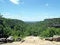 View into a river valley from a rock outcropping, with green forest below and blue sky above