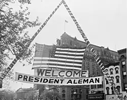Fotografía de la bandera estadounidense y una pancarta de bienvenida colgada sobre una calle de Washington, D.C. durante las ceremonia de honor de la visita del Presidente mexicano Miguel Alemán Valdés, 1947.