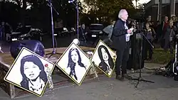 Orador frente al público. En el estrado tres imágenes de las muchachas.