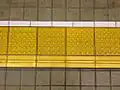 Pavimentos podotáctiles instalados en una plataforma, en una estación de trenes japonesa. El pavimento horizontal podotáctil, en la parte inferior, indica el lado «interior», alejado de las vías del tren.