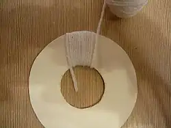 Se envuelve el anillo de cartón con el hilo, pasando por el agujero central el extremo del hilo elegido.