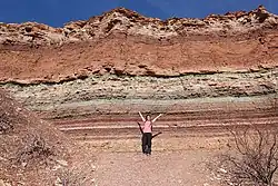 Fotografía de una mujer delante de estratos policromáticos en la Quebrada de Cafayate, provincia de Salta, Argentina.