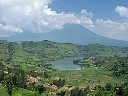 Fotografía de un lago con uno de los Montes Virunga detrás, parcialmente cubierto por nubes