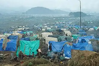 Vista de un campamento de refugiados en un día neblinoso, mostrando tiendas de varios colores y los refugiados