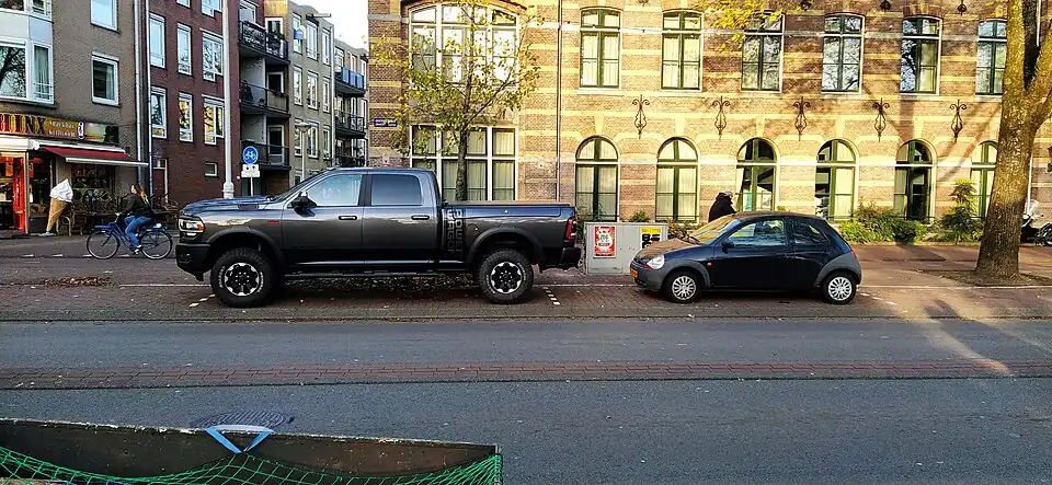 SUV de grandes dimensiones aparcado en la calle Compagniestraat, Ámsterdam (Países Bajos). Se observa cómo, a diferencia que el turismo que lo acompaña, el SUV se sale tanto por delante como por detrás de la plaza pintada.