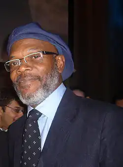 A middle-aged man, wearing a blue hat, glasses and a suit.