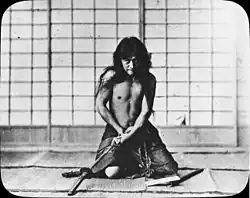 Fotografía de finales del siglo XIX que muestra a un samurai arrodillado en actitud de cometer seppuku.