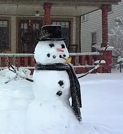 Un muñeco de nieve clásico en Winona Lake, Indiana, Estados Unidos. Translate It has coal eyes, a carrot nose, a top hat, a corncob pipe, a scarf, and branch arms. Tiene ojos de carbón, nariz de zanahoria, sombrero de copa, pipa de maíz, bufanda y brazos de rama.