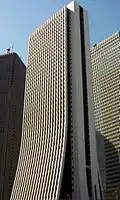 Ground-level view of a thin, white high-rise; the two wider sides curve and flair out at the bottom