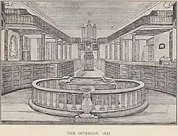 El interior de la iglesia lleno de mobiliario, que son bancas de caja, con galerías por encima, y en el primer plano el altar