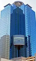 Ground-level view of a blue, glass high-rise; a circular pad sits atop the structure