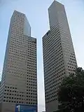 Ground-level view of two identical 45-storey towers with rectangular cross sections; a diagonal cut-out is present on each tower near the 30th floor
