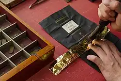 Sobre la tela que cubrirá el lomo de un libro, dos manos manipulan una herramienta para grabar tipos y guardas en oro.