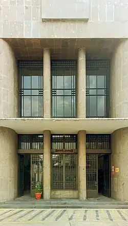 La fachada de un edificio con dos plantas cuya puerta principal está flanqueado por dos pilares.