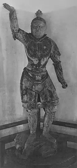 Tamonten, one of the Four Heavenly Kings in the Kaidan Hall. Portrait of a statue in front view. The right arm is raised, the hair sculpted with a top knot and the breast with armour. Narrow slit eyes and a facial expression as if frowning.