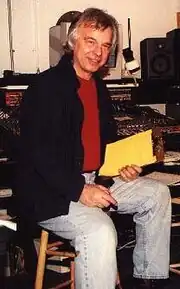 A gray-haired man with glasses and a black shirt standing in front of a microphone