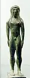 Estatuilla votiva realizada en bronce, de un joven desnudo con los brazos a los lados, proveniente de Chiusi (550-530 a. C.).