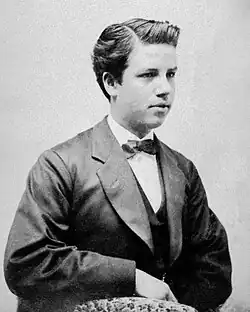 Fotografía en blanco y negro de un adolescente vistiendo traje oscuro y corbata de lazo.